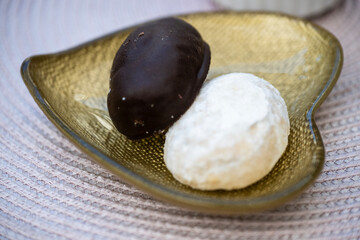 Two cookies—one chocolate-coated, one powdered—rest elegantly on a golden leaf-shaped dish atop a textured surface.