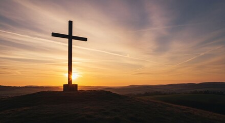 A silhouette of a Christian cross stands prominently on a hilltop against a breathtaking sunset sky, with warm orange and yellow hues illuminating the horizon.