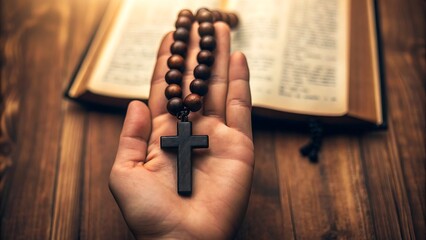 Hand holding wooden rosary with christian cross and bible on wooden table
