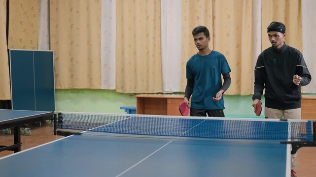 Focused indoor table tennis practice where two young players with rackets face one opponent, rallying ball across table while demonstrating teamwork and energy during competitive training session
