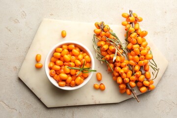 Fresh sea buckthorn berries in bowl and leaves on beige table, flat lay
