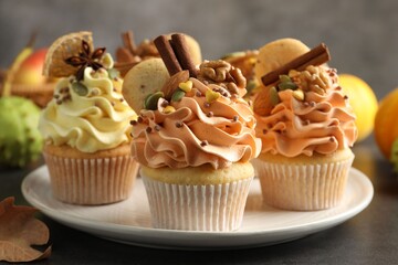Delicious cupcakes with colorful cream, spices, nuts and autumn decor on grey table, closeup