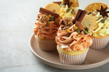 Delicious cupcakes with colorful cream, spices and nuts on grey table, closeup. Space for text
