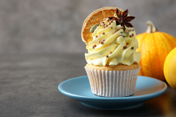 Delicious cupcake with color cream, anise, dried orange and autumn decor on grey table, closeup. space for text