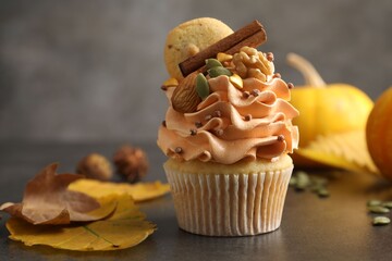 Delicious cupcake with color cream, cinnamon, cookie, nuts and autumn decor on grey table, closeup