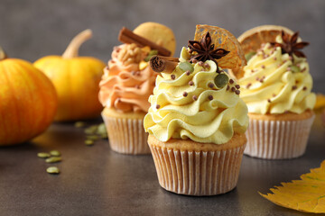 Delicious cupcakes with colorful cream, spices and autumn decor on grey table, closeup