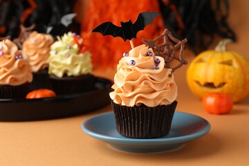 Delicious cupcake with chocolate web, bat topper and sprinkles on orange table against color background, closeup with space for text. Halloween celebration