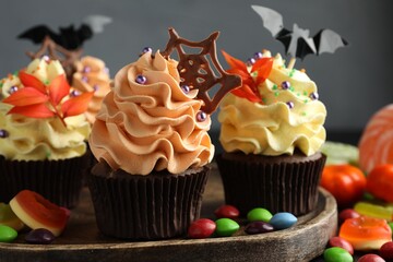 Delicious cupcakes with bat toppers, sprinkles, chocolate web and colorful candies on dark table against grey background, closeup. Halloween celebration