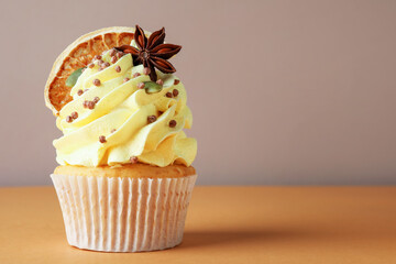Delicious cupcake with sprinkles and spices on coral table against grey background, closeup with space for text. Autumn atmosphere