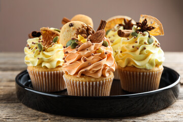 Delicious cupcakes with sprinkles, nuts and spices on wooden table against grey background, closeup. Autumn atmosphere