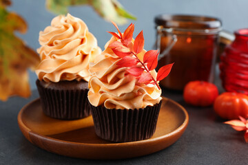 Delicious cupcakes with branch with red leaves on grey textured table against light blue background, closeup. Autumn atmosphere