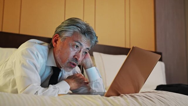Male business person looking at laptop in bed
