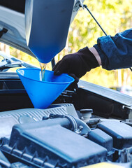 Close-up of a man pouring engine oil into a car engine.