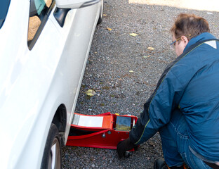 A man jacks up a passenger car for repairs on the street.
