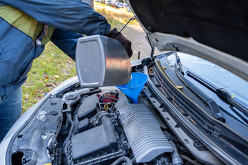 Close-up of a man pouring engine oil into a car engine.