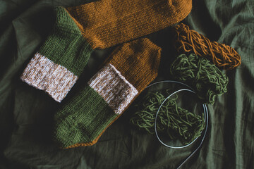 Cozy knitted socks with yarn ball and knitting needles. Striped wool socks on dark green sheet....