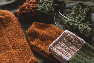 Cozy knitted socks with yarn ball and knitting needles. Striped wool socks on dark green sheet....