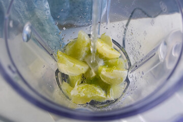 Woman adding water to lime pieces in blender preparing cooking brazil lemonade on kitchen at home. Recipe cuisine culinary. Prepare citrus fruit dessert homemade fresh beverage.