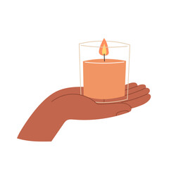 A hand holds a lit orange candle in a glass container