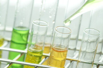 Laboratory glassware with dropper dripping liquid into test tube with light blue liquid close up macro photography.
