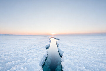 Obraz premium A narrow crack in a vast frozen ice sheet reveals dark water beneath during a serene sunset.