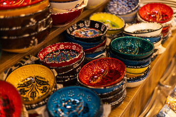 Brightly colored ceramic bowls of various designs are neatly arranged on wooden shelves in a...