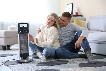 Happy couple near electric heater on floor at home