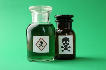 Bottles of poison with warning signs on green background, closeup