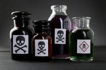 Bottles of poison with warning signs on black wooden table, closeup