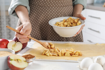 Making delicious apple strudel. Woman putting pieces of fruit onto dough at table in kitchen, closeup