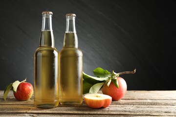 Delicious cider in glass bottles and apples on wooden table against dark gray background. Space for text