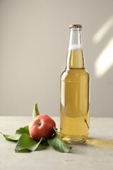 Delicious cider in glass bottle and apples on gray table against light background