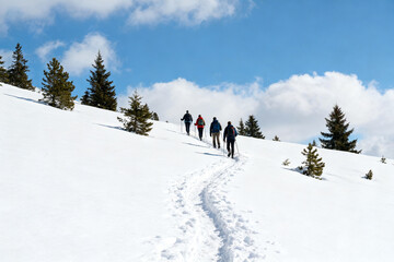 Group of hikers walking uphill on a snowy slope under a clear blue sky