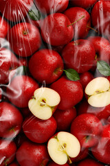 Fresh red apples with water drops and sliced halves wrapped in transparent packaging