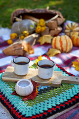 Cozy autumn picnic in the garden with pumpkins, colorful leaves, hot tea in enamel mugs, candlelight and warm blanket. Rustic fall atmosphere, relaxation and seasonal outdoor decoration