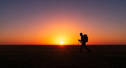 Fototapeta premium Silhouette of a lone hiker with a backpack walking across a vast, flat landscape at sunset.