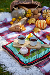 Cozy autumn picnic in the garden with pumpkins, colorful leaves, hot tea in enamel mugs, candlelight and warm blanket. Rustic fall atmosphere, relaxation and seasonal outdoor decoration
