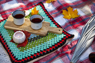 Cozy autumn picnic in the garden with pumpkins, colorful leaves, hot tea in enamel mugs, candlelight and warm blanket. Rustic fall atmosphere, relaxation and seasonal outdoor decoration