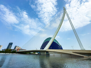 Obraz premium Stunning modern bridge with unique architecture over tranquil water under a bright blue sky in a vibrant city