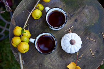 Two white enamel mugs with hot tea on a rustic wooden table in the garden, decorated with quince...