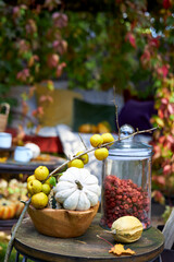 Cozy autumn still life in a garden with rustic table, pumpkins, quinces, glass jar, and warm seasonal decor. Outdoor fall atmosphere with natural colors, homely comfort, and countryside charm, perfect