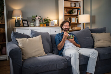 Obraz premium Man relaxing on couch eating healthy salad