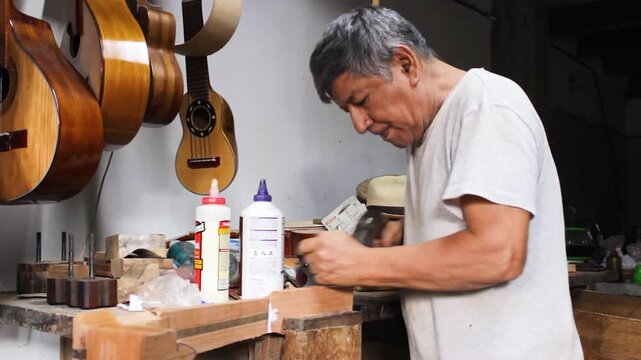 An elderly Colombian man polishes a wooden board with a specialized carpenter's plane inside a lutherie workshop in Neiva, Huila, Colombia. Concept of handmade 