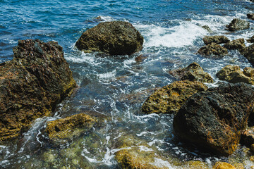 Waves crash against rugged rocks at a tranquil coastal landscape under the bright sun near the shoreline
