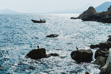 Boaters navigate shimmering waters near rocky coastline under a clear sky at midday