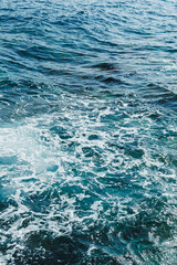 Waves crashing on a serene ocean surface during a sunny afternoon near the coast