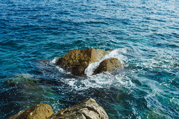 Waves crashing over rocky shoreline under bright sunlight creating a serene coastal scene