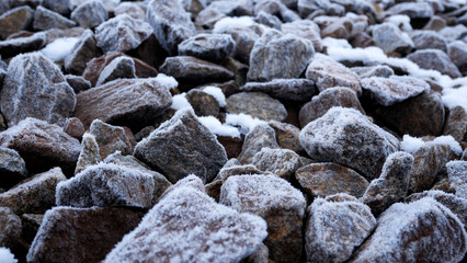 Many natural stones covered with frost on a cold winter day. Close-up texture of frozen stones. Winter background with icy surface.