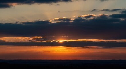 Obraz premium The sun peeks through dark clouds at sunset, casting orange and yellow rays across the sky.