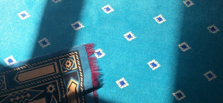 A blue prayer mat is placed on a patterned blue carpet in a daytime setting